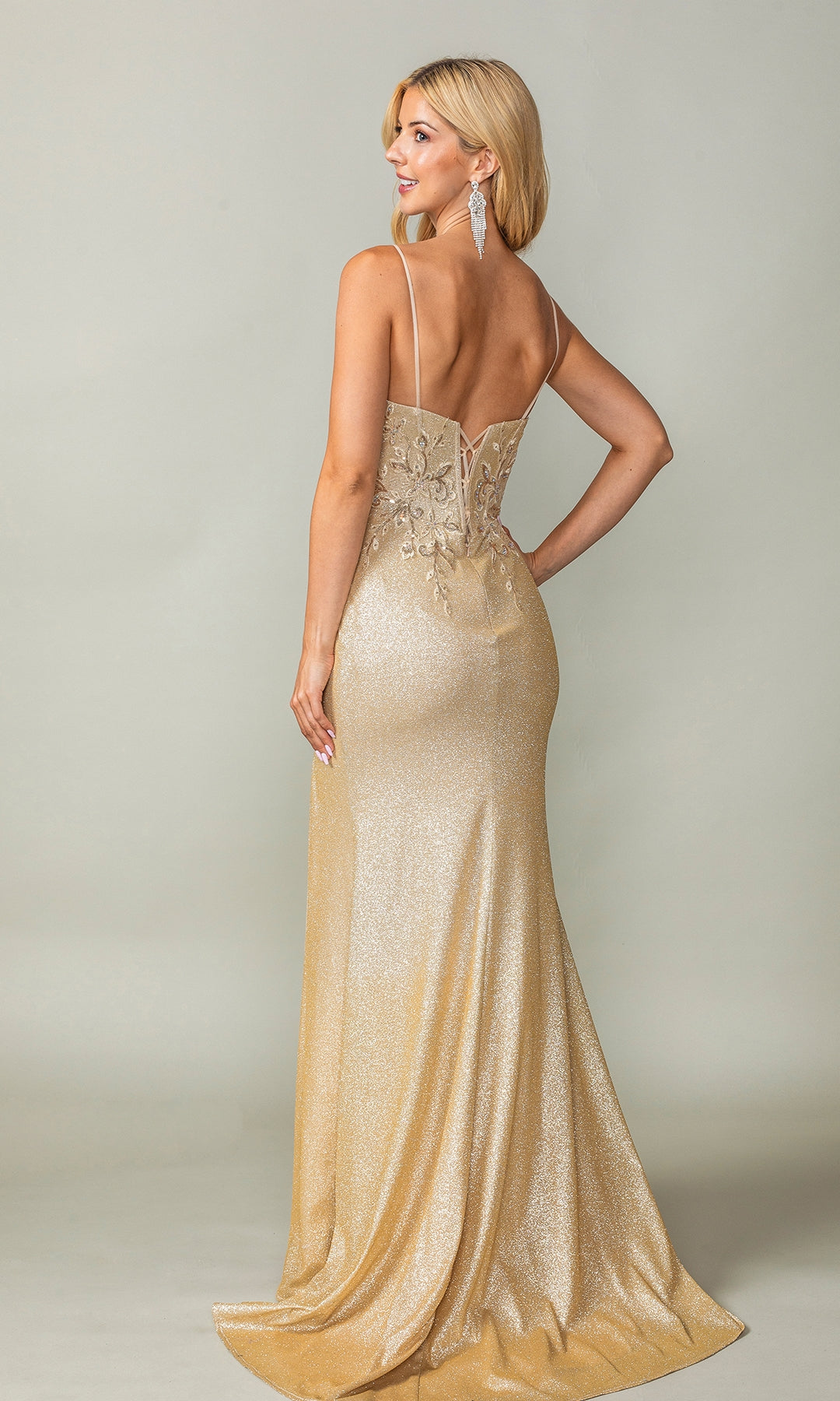 A woman poses in the Long Glitter Prom Dress: Dancing Queen 4375, a floor-length gold gown with thin straps and intricate back detailing.